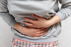 Close de mulher com as duas mãos na região abdominal e o tronco curvado indicando uma dor abdominal devido a uma retocolite ulcerativa